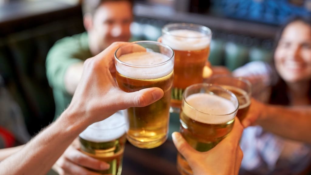 A group of people sitting together, each raising a glass of beer in a toast, perhaps celebrating their new insights into the various types of liquor licenses in California.